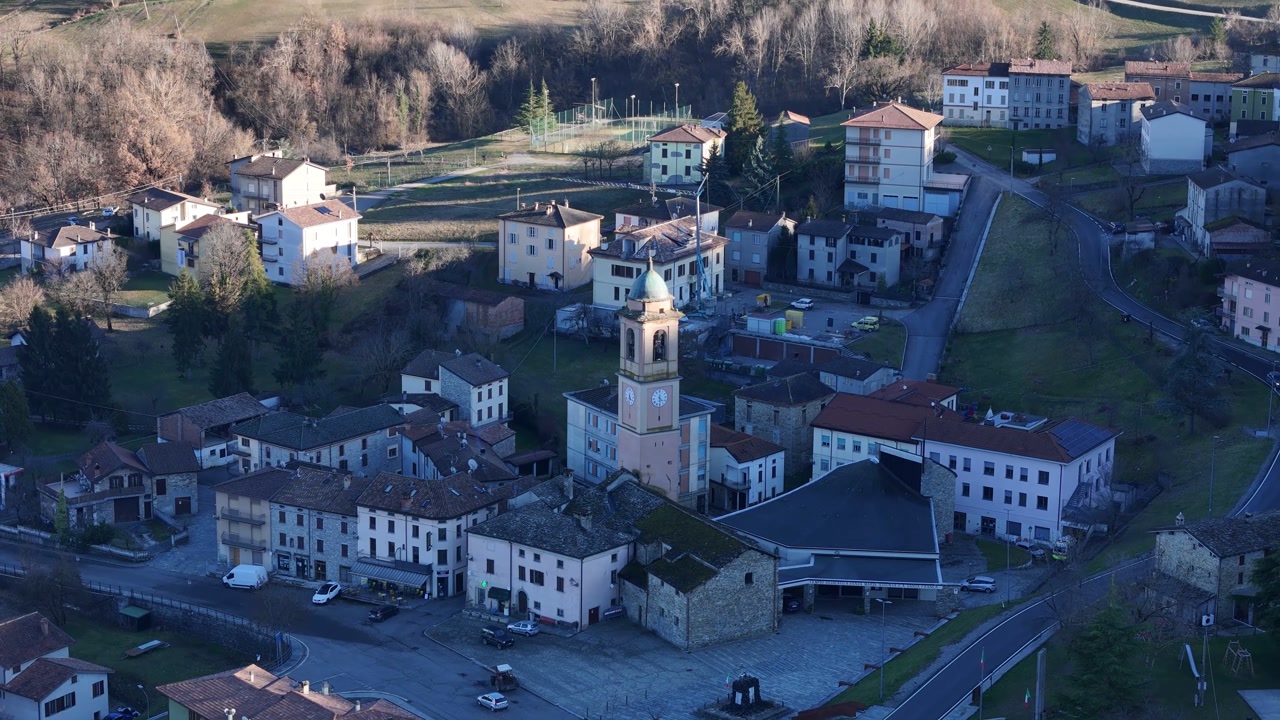 Drone slowly ascends over Morfasso PC picturesque Italian village, revealing a central piazza, church, and surrounding residential buildings nestled in a valley