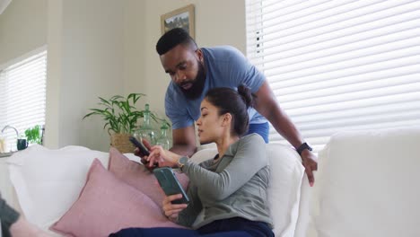 Pareja-Diversa-Usando-Teléfonos-Inteligentes-Y-Hablando-En-La-Sala-De-Estar-De-Casa,-En-Cámara-Lenta