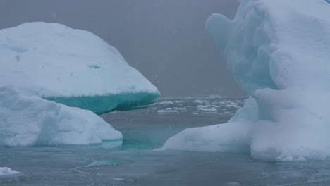 antarctica coast on snowy day, icebergs in cold ocean water, snowfall and mist