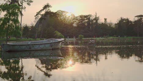 A-static-shot-of-an-abandoned-boat-in-the-middle-of-the-lake-of-the-Vincennes-Woods-Parc-at-sunset-in-Paris,-France