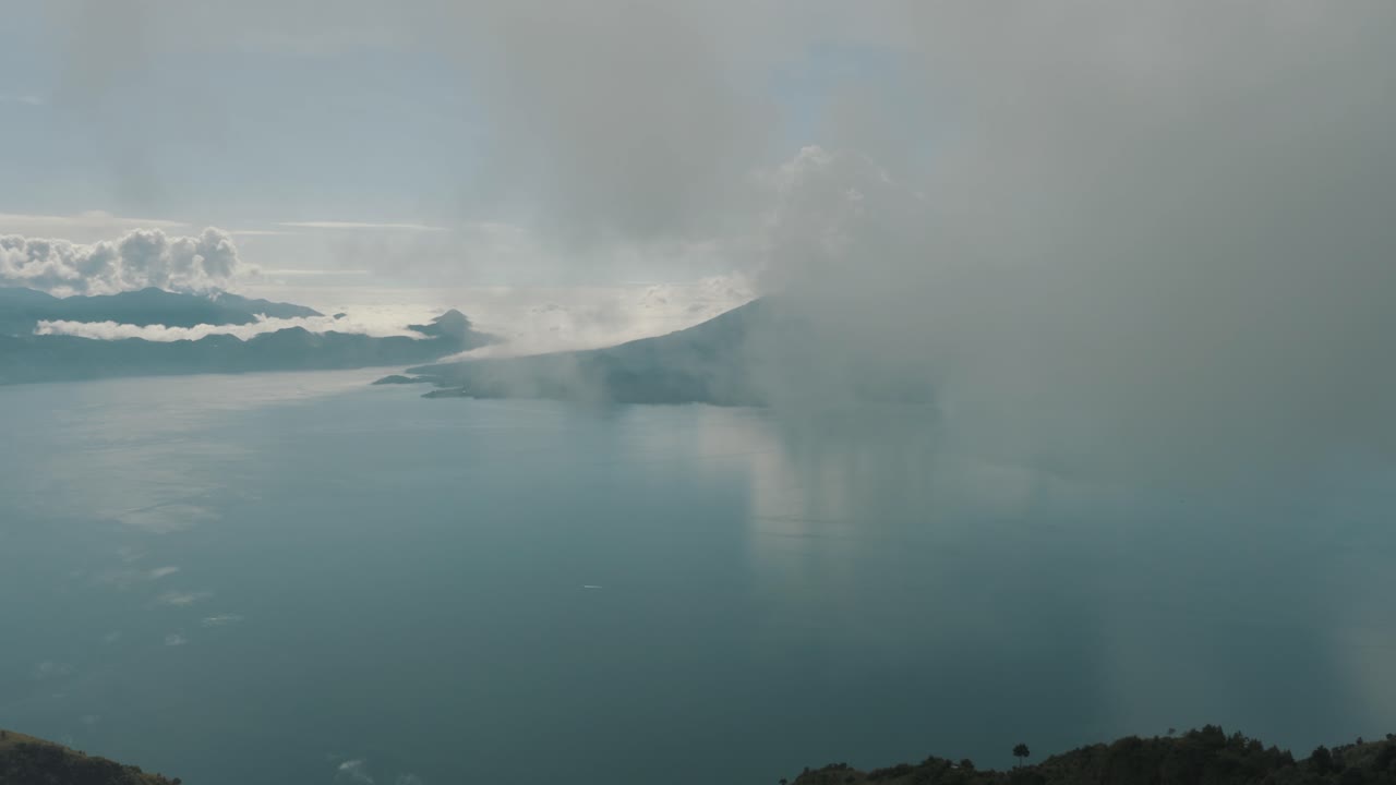 drone aéreo volando alto a través de las nubes revelando el hermoso lago azul de atitlán en guatemala