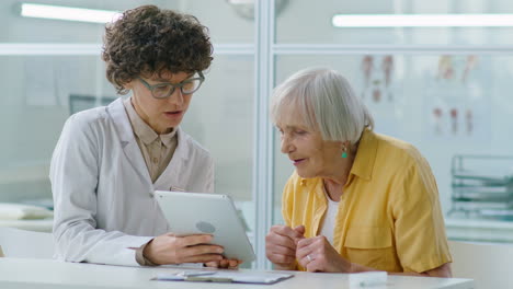 female doctor using tablet and consulting elderly woman