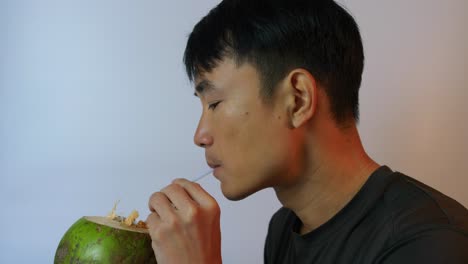 close up of a southeast asian young man drinking in slow motion through a coconut straw