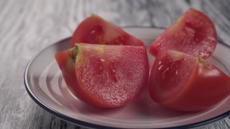 four slices of sliced juicy tomato on a white plate with a blue border on a wooden texture table