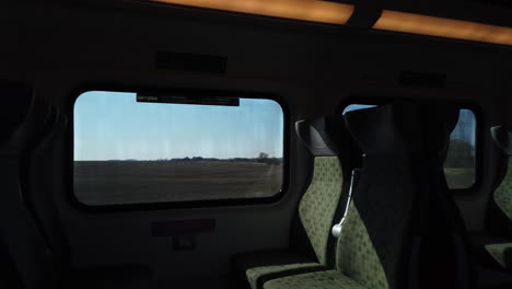 travellers perspective from the interior of a moving train, looking out to the countryside passing by