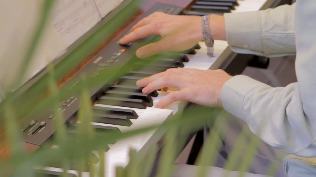 Hands playing piano keys through greenery