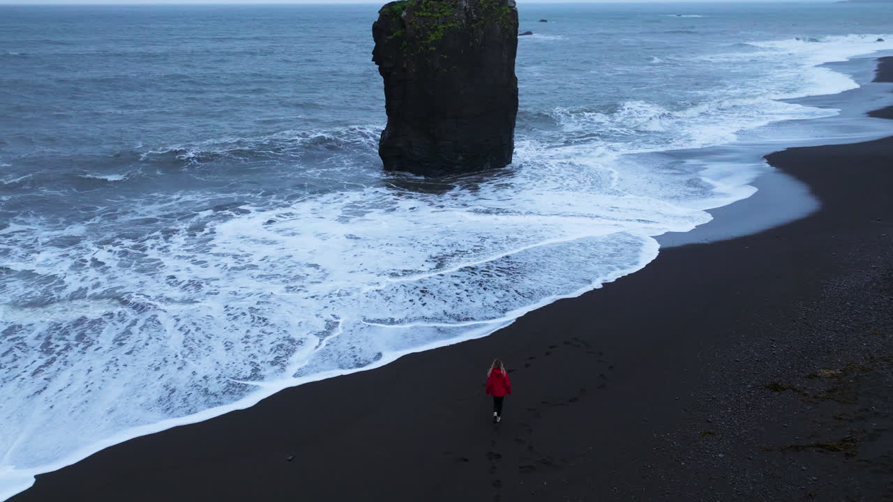mujer con chaqueta roja caminando por la playa de laekjavik hasta el océano en islandia