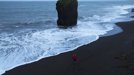 Frau-In-Roter-Jacke-Zu-Fuß-Am-Strand-Von-Laekjavik-Zum-Meer-In-Island