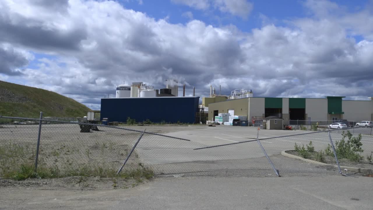 Smoke streama out of a modern factory on a blue sky day with a broken fence at the entrance