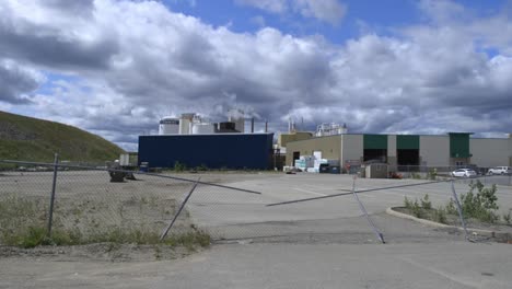 smoke streama out of a modern factory on a blue sky day with a broken fence at the entrance