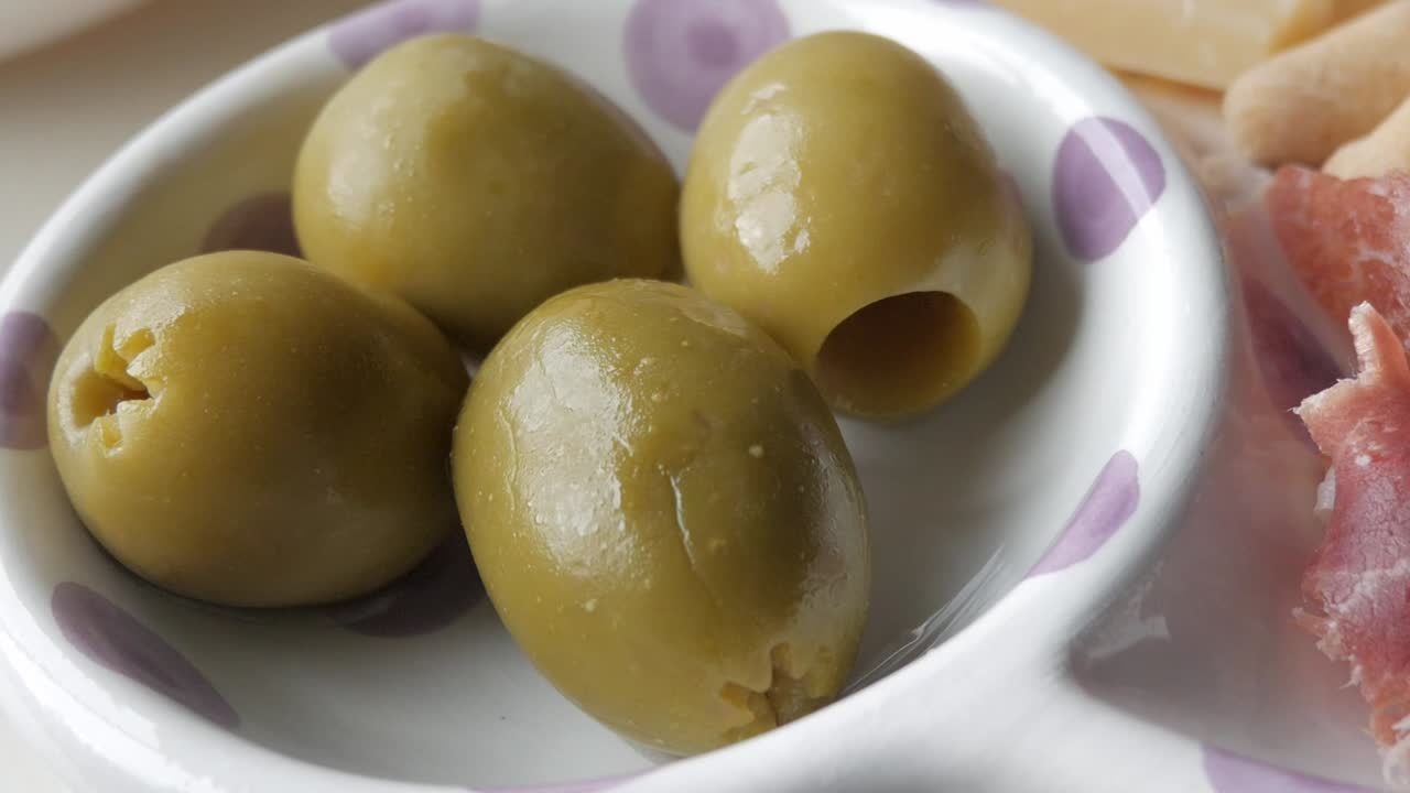 Green olives on a small dish, part of a tapas selection including jamon, cheese, and chips