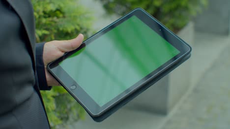 hombre de negocios navegando por internet en línea en una tableta digital al aire libre. hombre de negocios de cerca trabajando en el touchpad en la calle. manos masculinas escribiendo en el pad con pantalla verde en cámara lenta.
