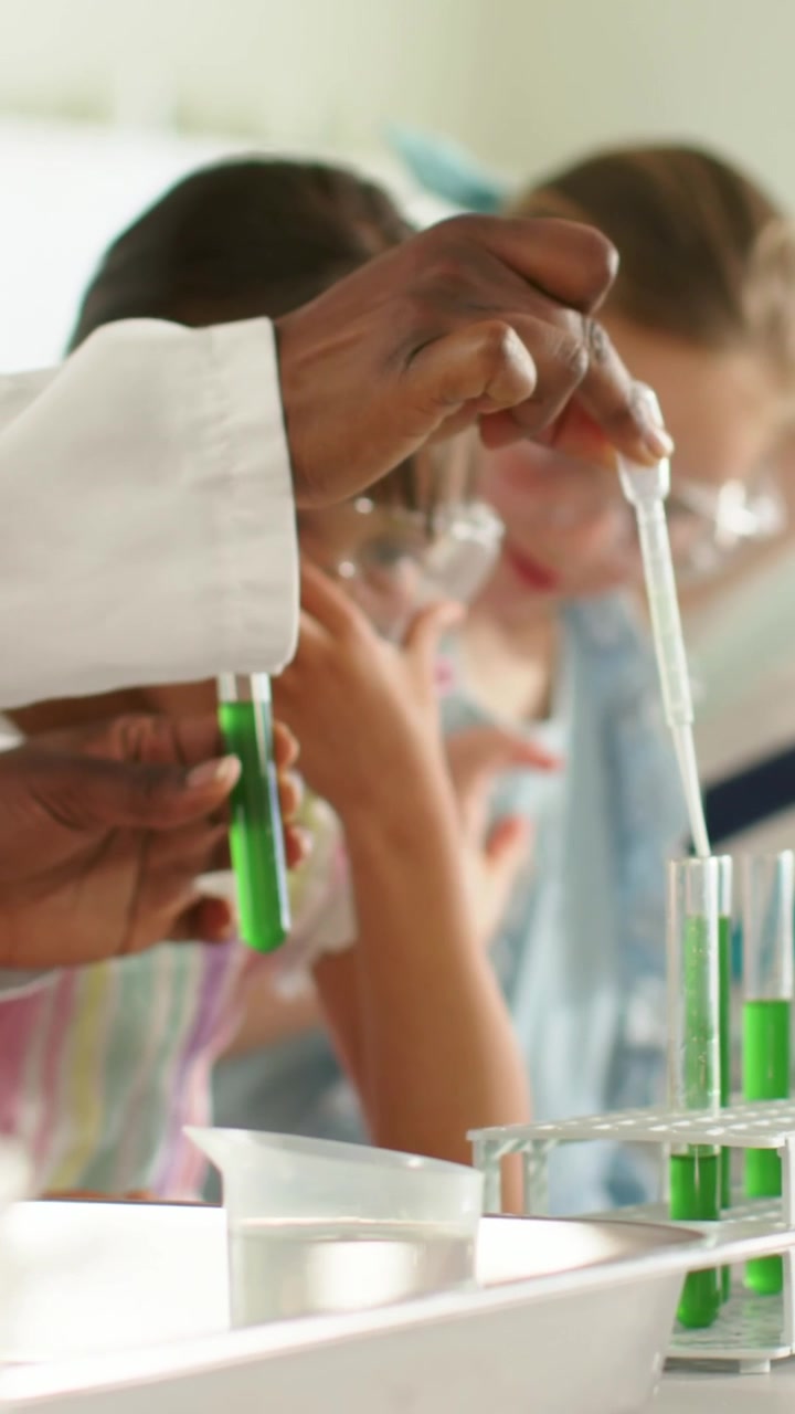Vertical video: Reaching with pipette labcoat teacher pipetting at school lab, kids wearing goggles