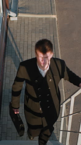 man black suit climbing office staircase holding briefcase with right hand, iron railing with left hand, sunlight reflecting off face, focused, professional, upward movement
