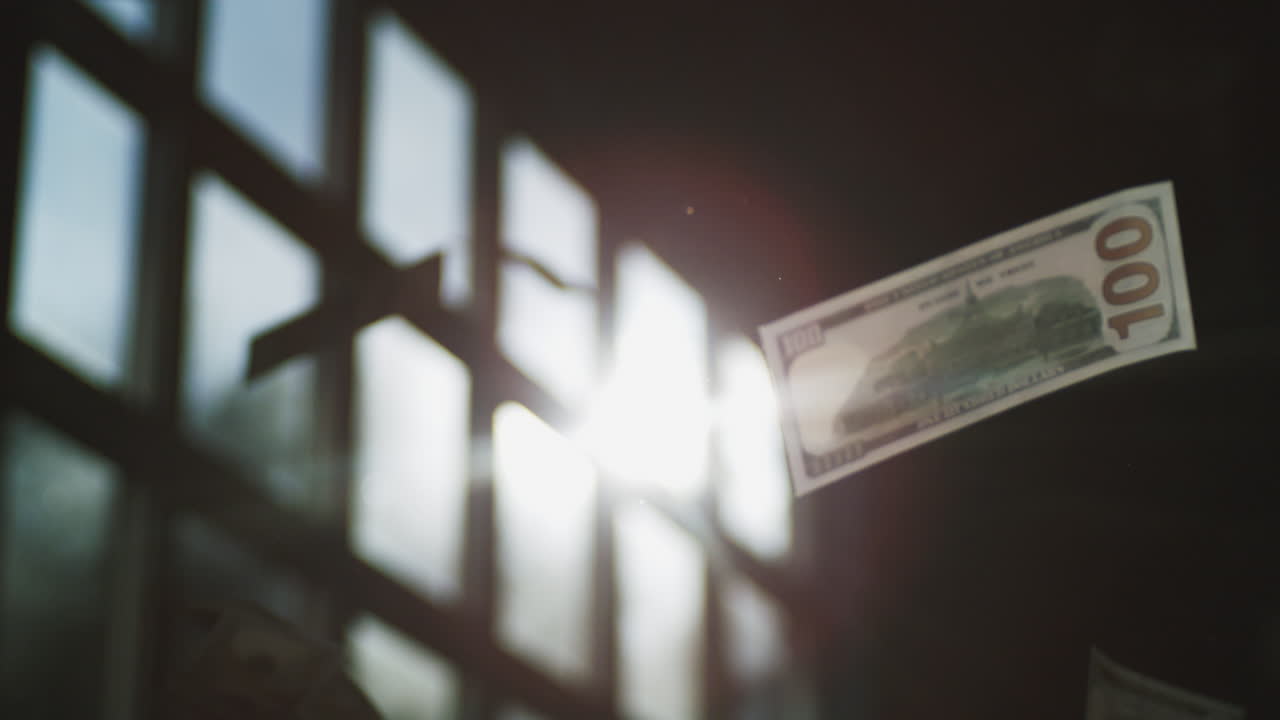 Hundrede dollarseddel flyvende i sollys gennem industrivinduer