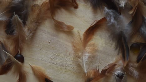 top view of a minimal background with soft and fluffy white, brown and black feathers falling, near some stones, on a light wooden background