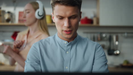 Portrait-focused-freelancer-working-home-while-blond-wife-dancing-on-backdrop