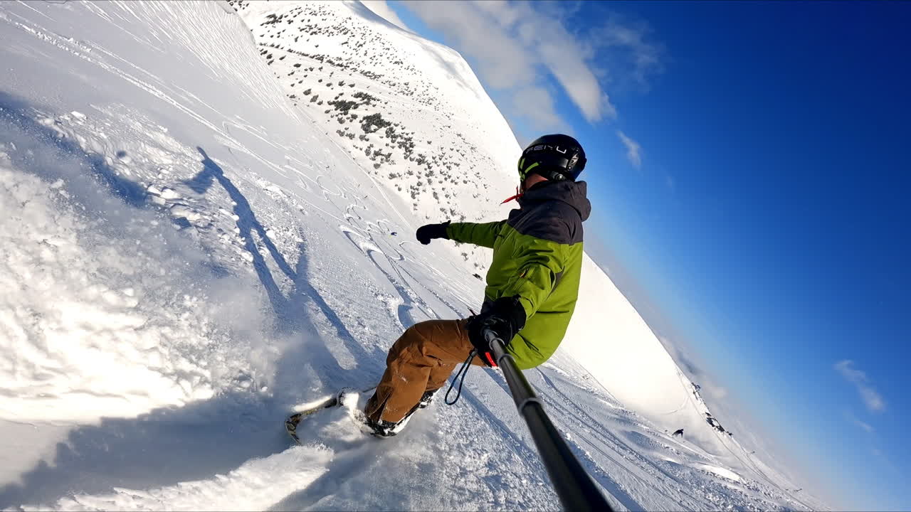 Taking selfie of the ride on the snowboard. Sportsman goes down the mountain slope recording his descend.