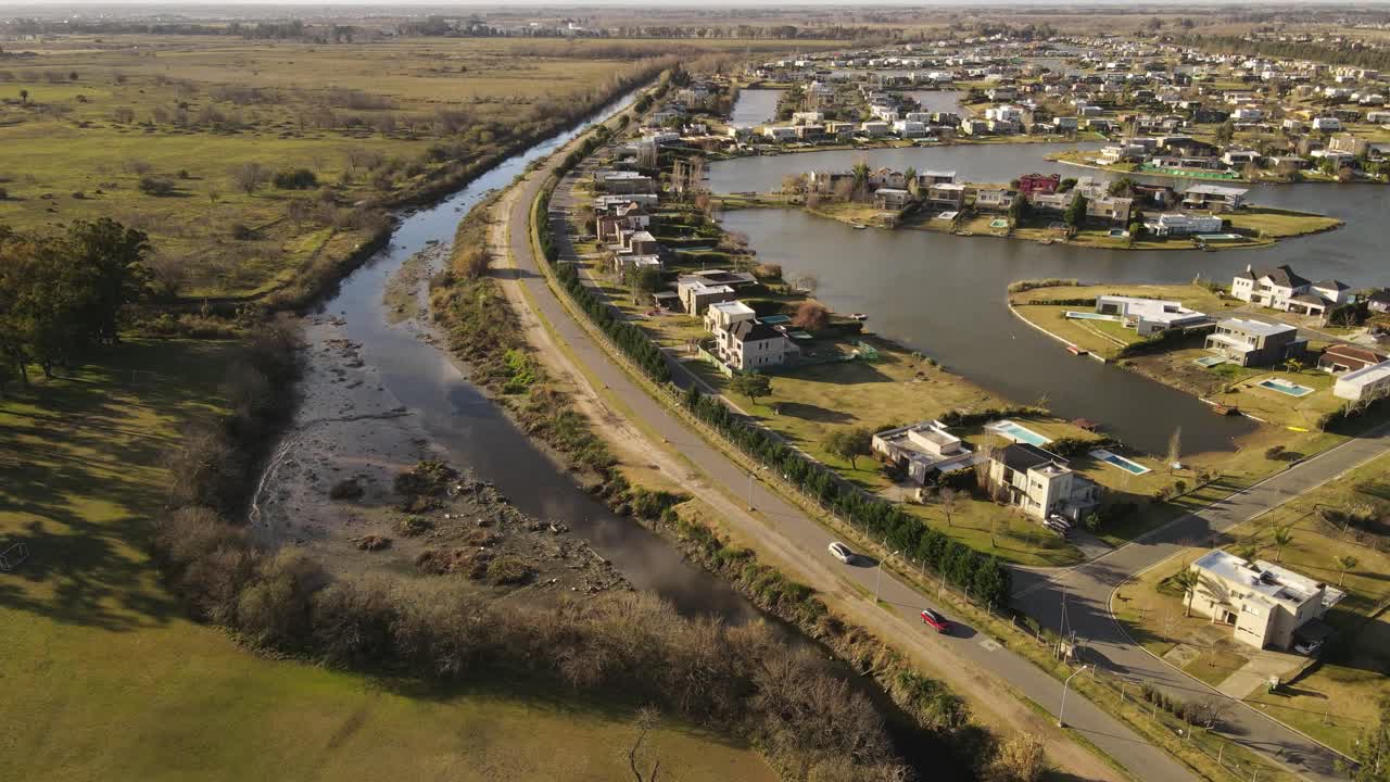 toma aérea de autos conduciendo en la carretera al lado de la isla del lago con muchas casas residenciales en buenos aires