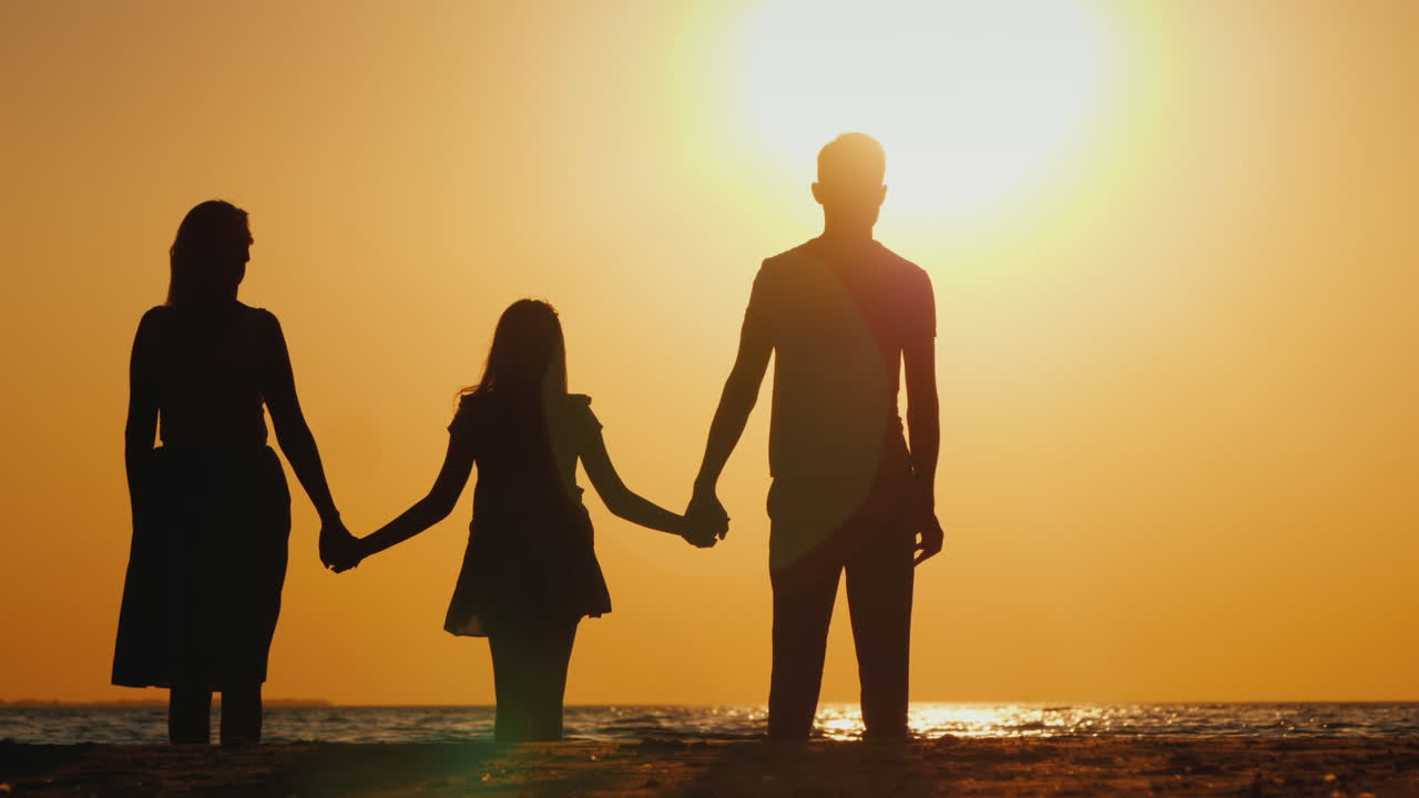 子供を持つ若い家族が寄り添い、一緒に海に沈む夕日を楽しみにしています