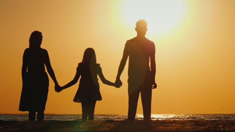 una familia joven con un niño se abraza y espera la puesta de sol sobre el mar para pasar un buen rato juntos