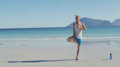 video de un hombre caucásico con rastas practicando yoga de pie en una playa soleada
