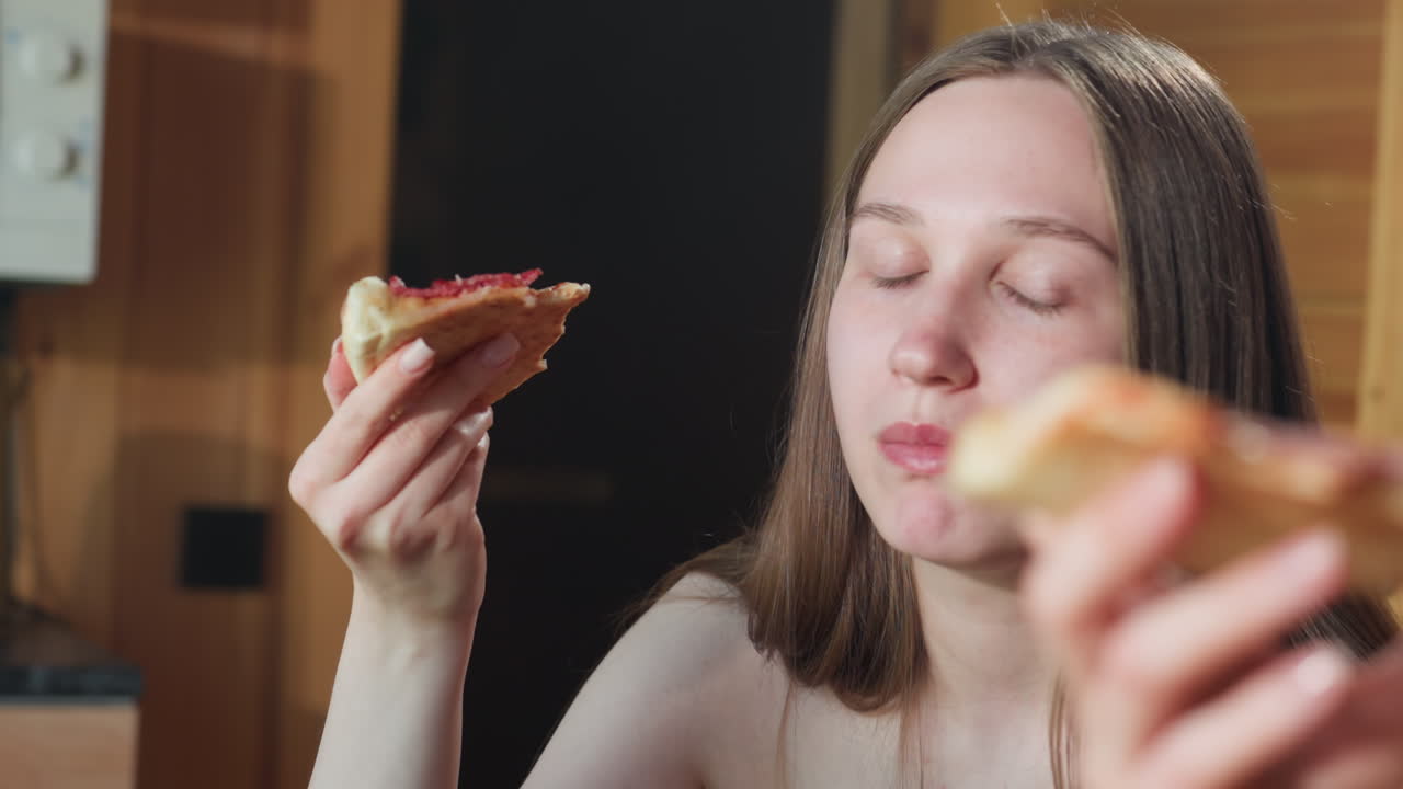 Young girl in towel enjoying a slice of pizza with a blissful expression, savoring the delicious food in a cozy indoor setting, captured in a relaxed atmosphere, she is having a good time