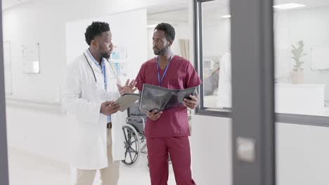 Busy-african-american-male-doctor-and-nurse-with-xray-and-tablet,-talking-in-slow-motion,-unaltered