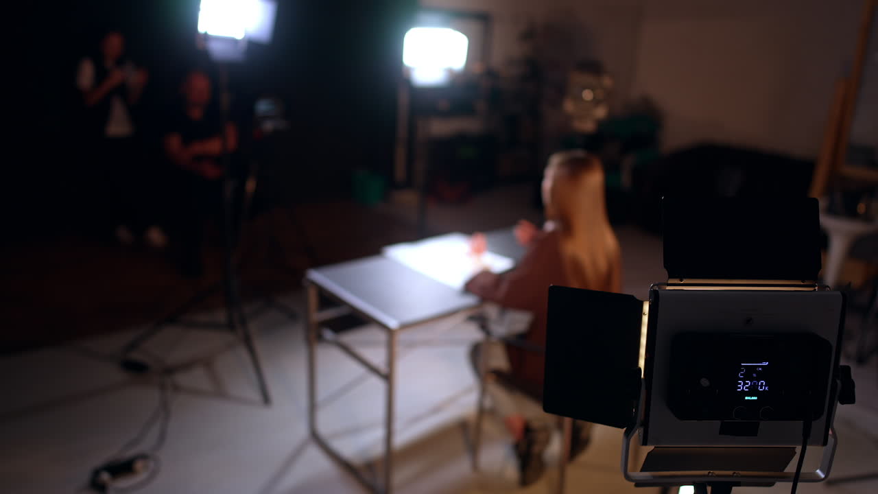 Soffit is illuminating a lady sitting at desk from behind. Footage in modern photo studio.