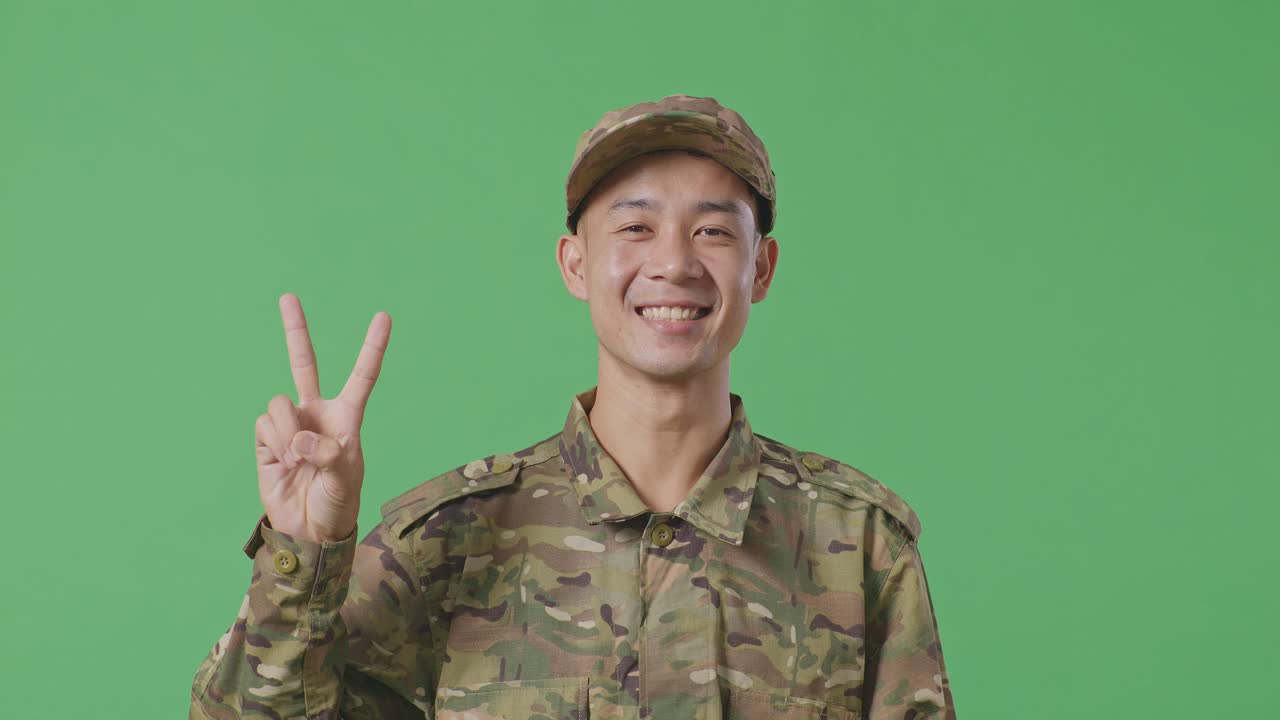 Close Up Of Asian Man Soldier Smiling And Showing Peace Gesture To Camera While Standing In The Green Screen Background Studio