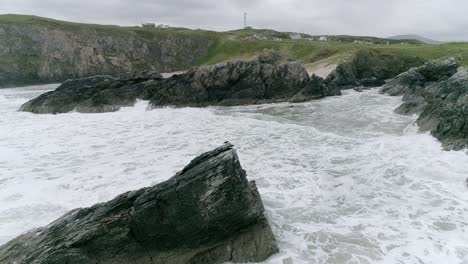 aerial tracking backwards from a harsh rocky and sandy coastline on a windy day