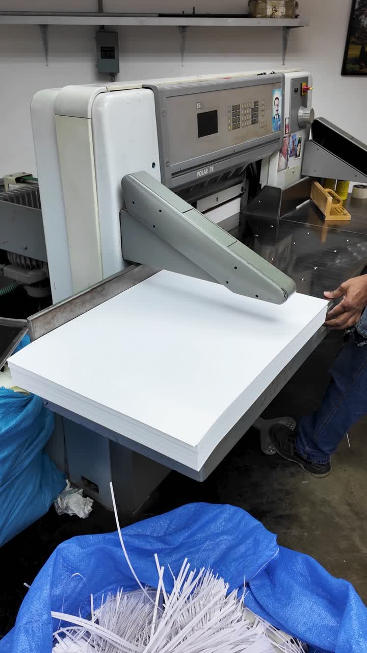 Large industrial paper cutting machine, Polar, with stack of white paper being processed by a man