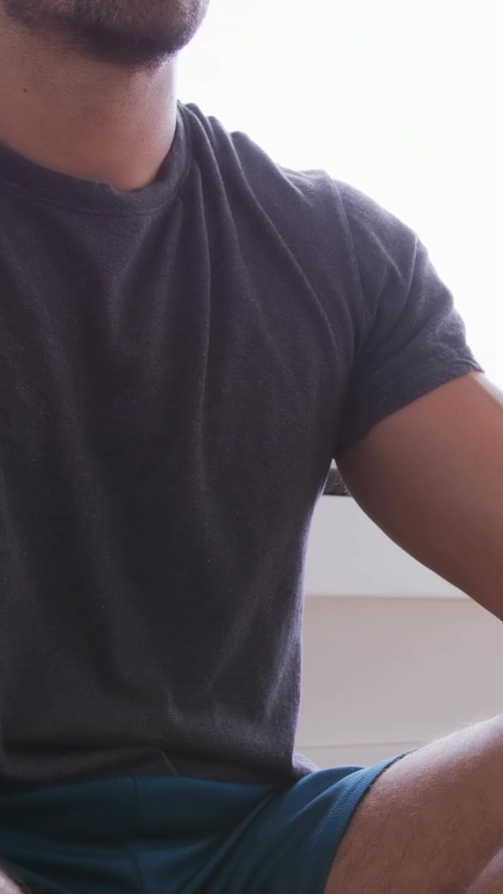 Video verticale: Uomo che indossa e prova un'esperienza VR a casa in maglietta grigia e pantaloncini verde acqua, con visore bianco