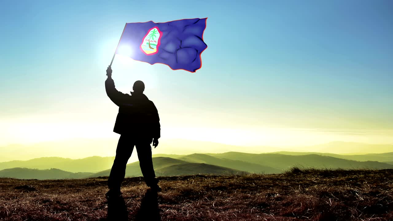 Uomo vincitore in silhouette di successo che sventola la bandiera di Guam in cima alla vetta della montagna. Sfondo Cinemagraph in LOOP.