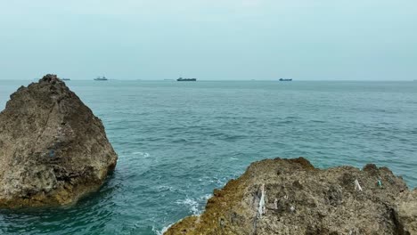 aerial forward shot of rocky shoreline and giant industrial container ship in background - taiwan south east asia