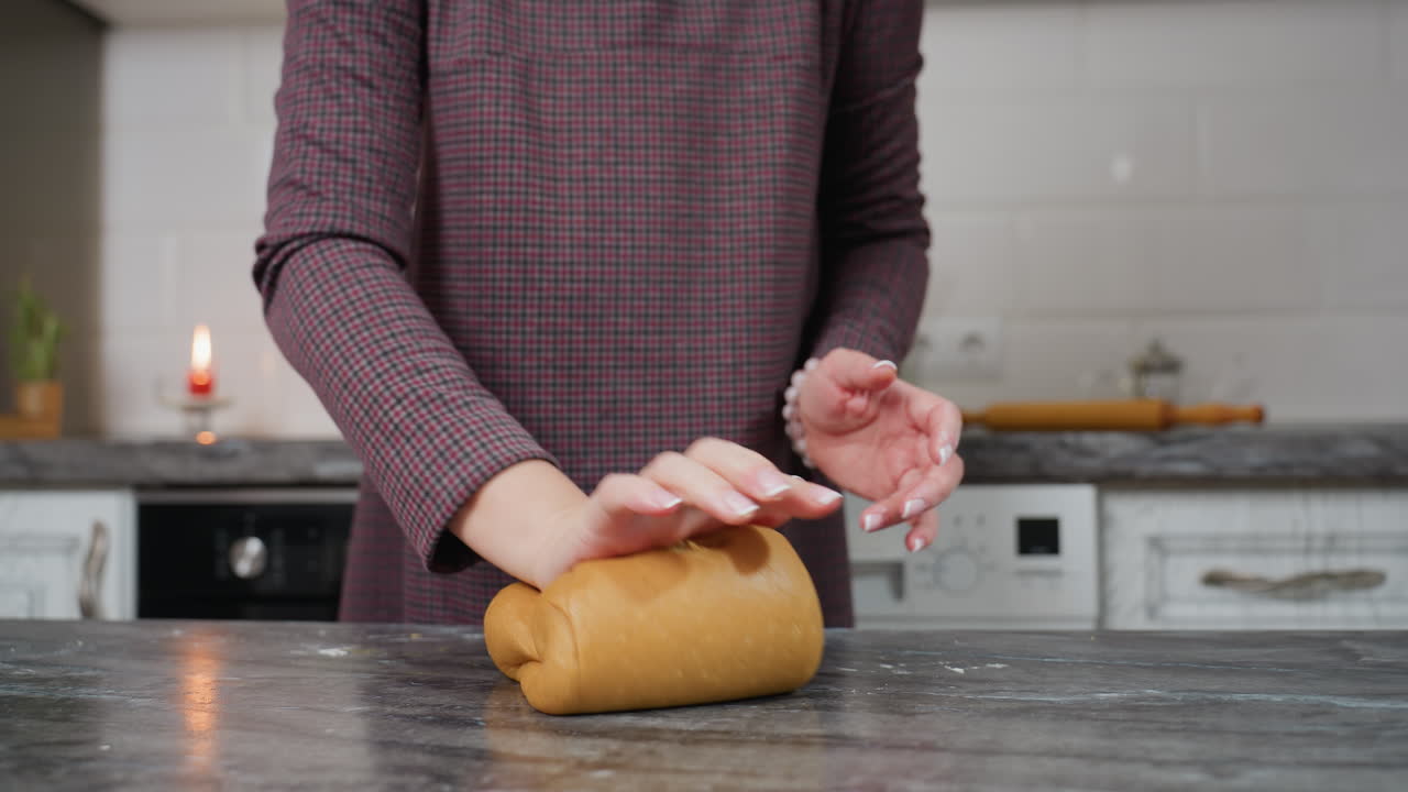 близкий взгляд на молодую женщину, носящую браслет, выпекающую тесто вручную на мраморной столешнице в кухонной обстановке с свечой, катушкой, посудой, создающей теплую уютную атмосферу для выпечки хлеба