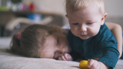 little girl hugs cute brother nibbling on yellow toy on bed