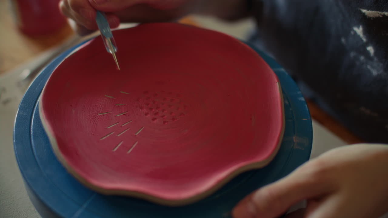 вЂ‹вЂ‹Hands of Ceramic Artist Engraving Lines on Red Glazed Plate with Scribe Tool