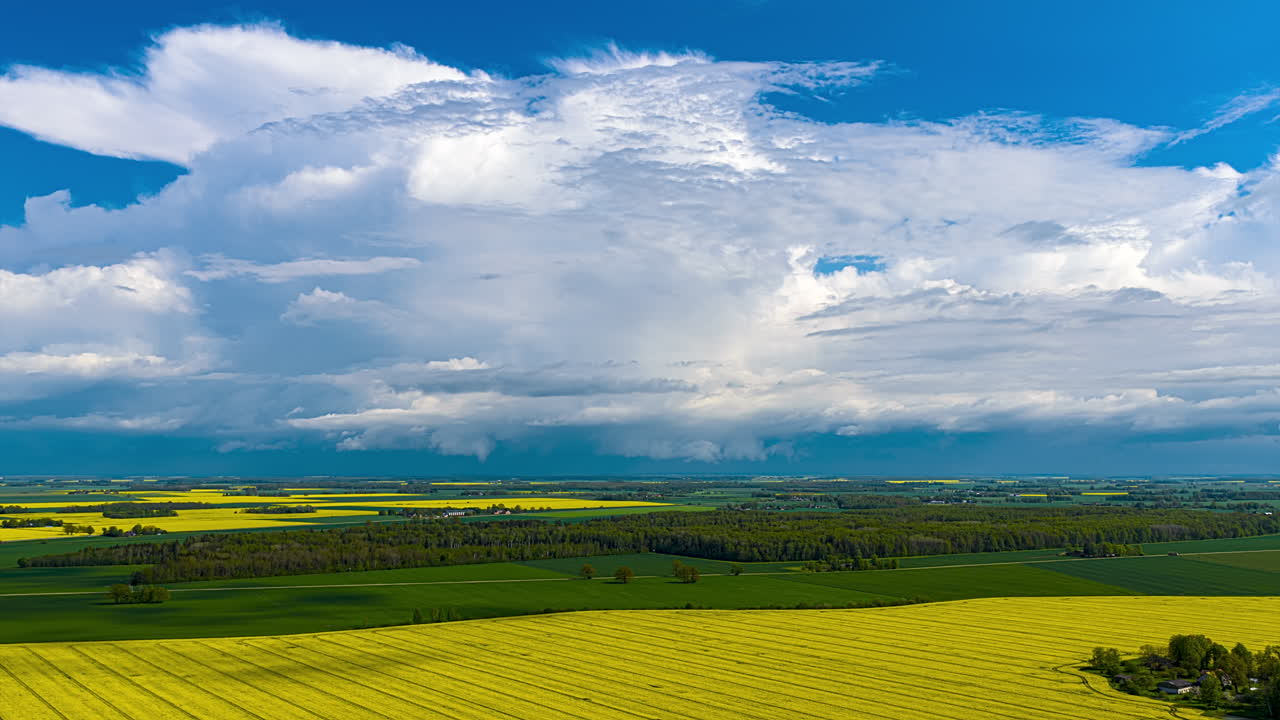 Yellow fields of rapeseed and other cash crops in rural Europe's countryside as clouds pass by in this colorful aerial cloudscape time lapse