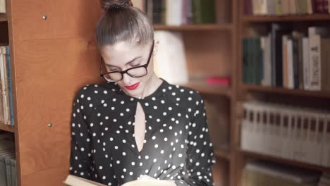 woman flicking through pages of a book while leaning against a shelf in a library