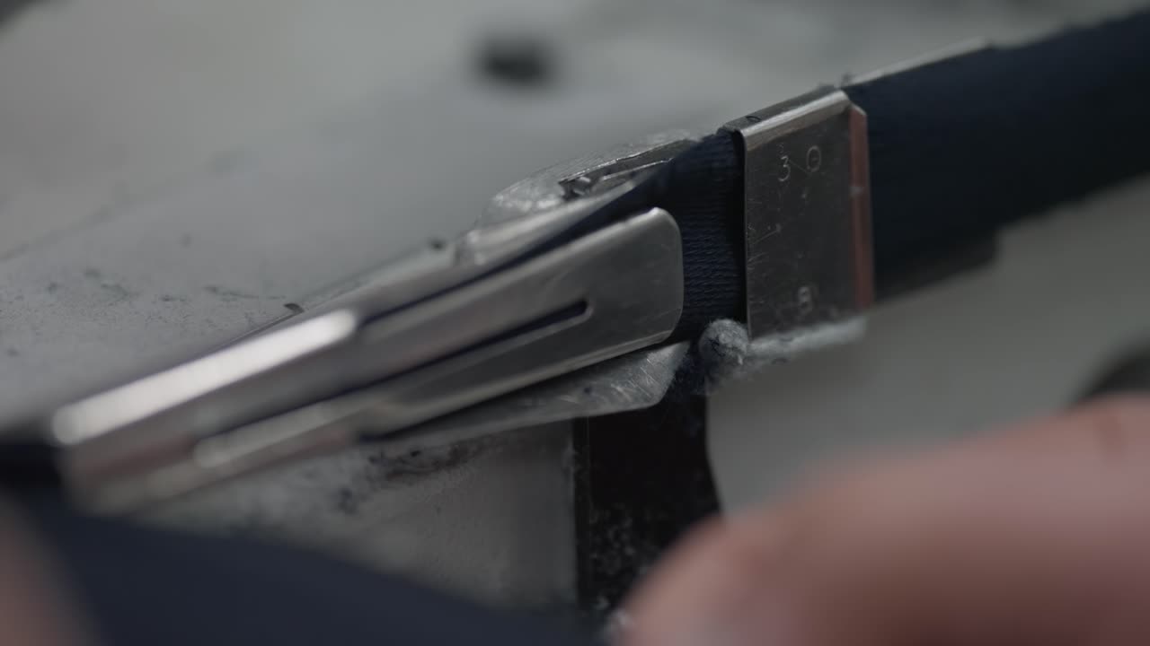 Primo piano di una macchina da cucire a punto copertura che guida il bordo del tessuto attraverso un dispositivo per bordare metallico.