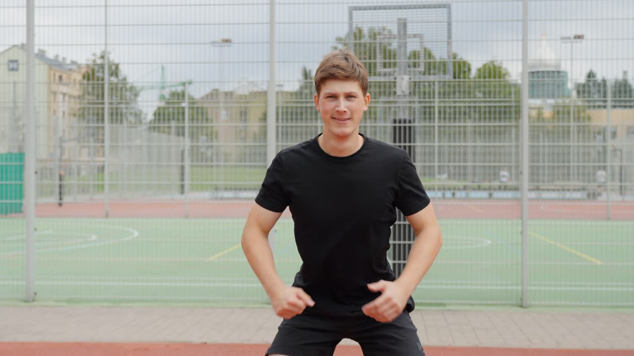 Medium shot of young man in black outfit performing squats on outdoor sports court