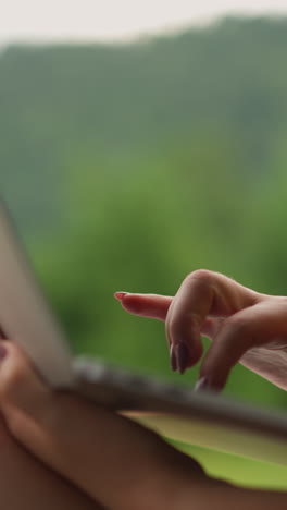 woman writes post for blog page on laptop computer sitting against misty mountain silhouettes at eco resort close side view slow motion