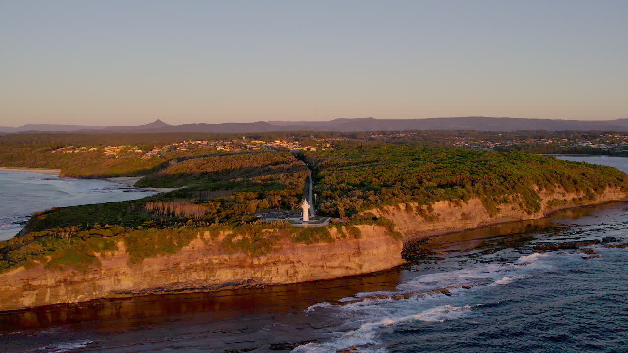 Calm view of the rocky coastline near Ulladulla, with Warden Head Lighthouse bathed in warm morning light. The peaceful scene highlights the rugged beauty and vastness of the coast.