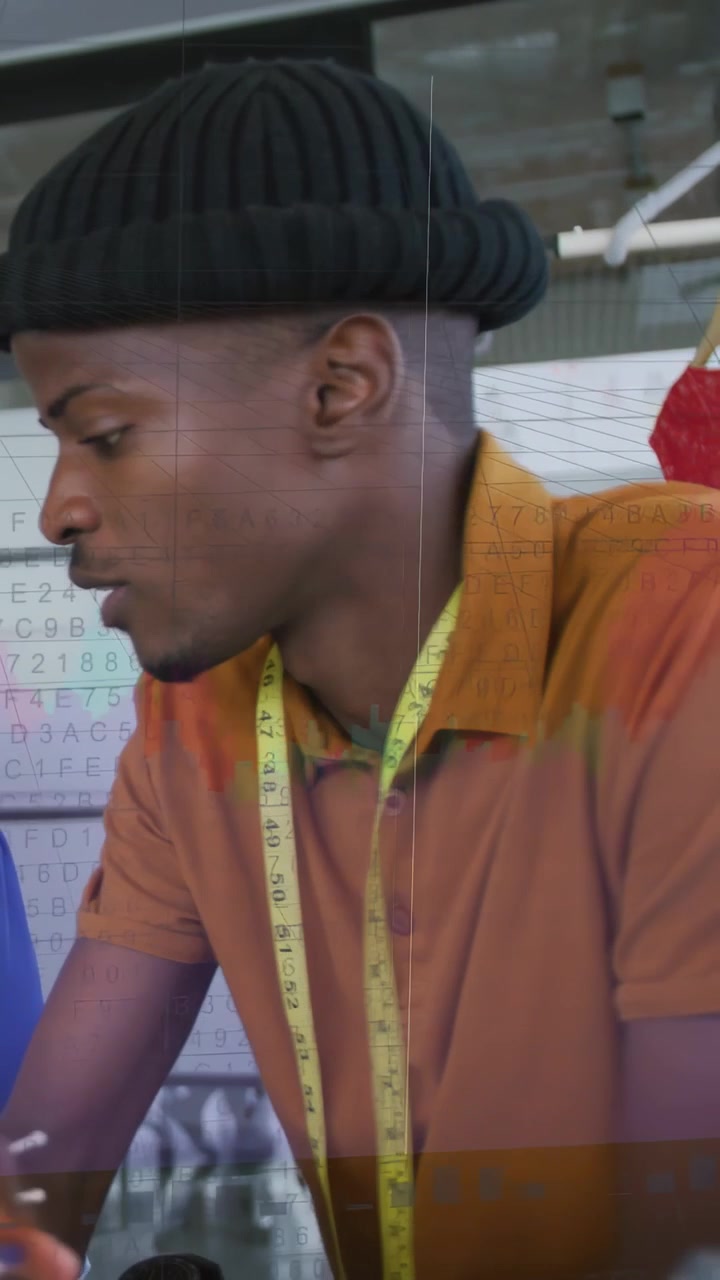 Vertical video: Tailor leaning at table on peer cue holding tape,pins checking fit as charts moving