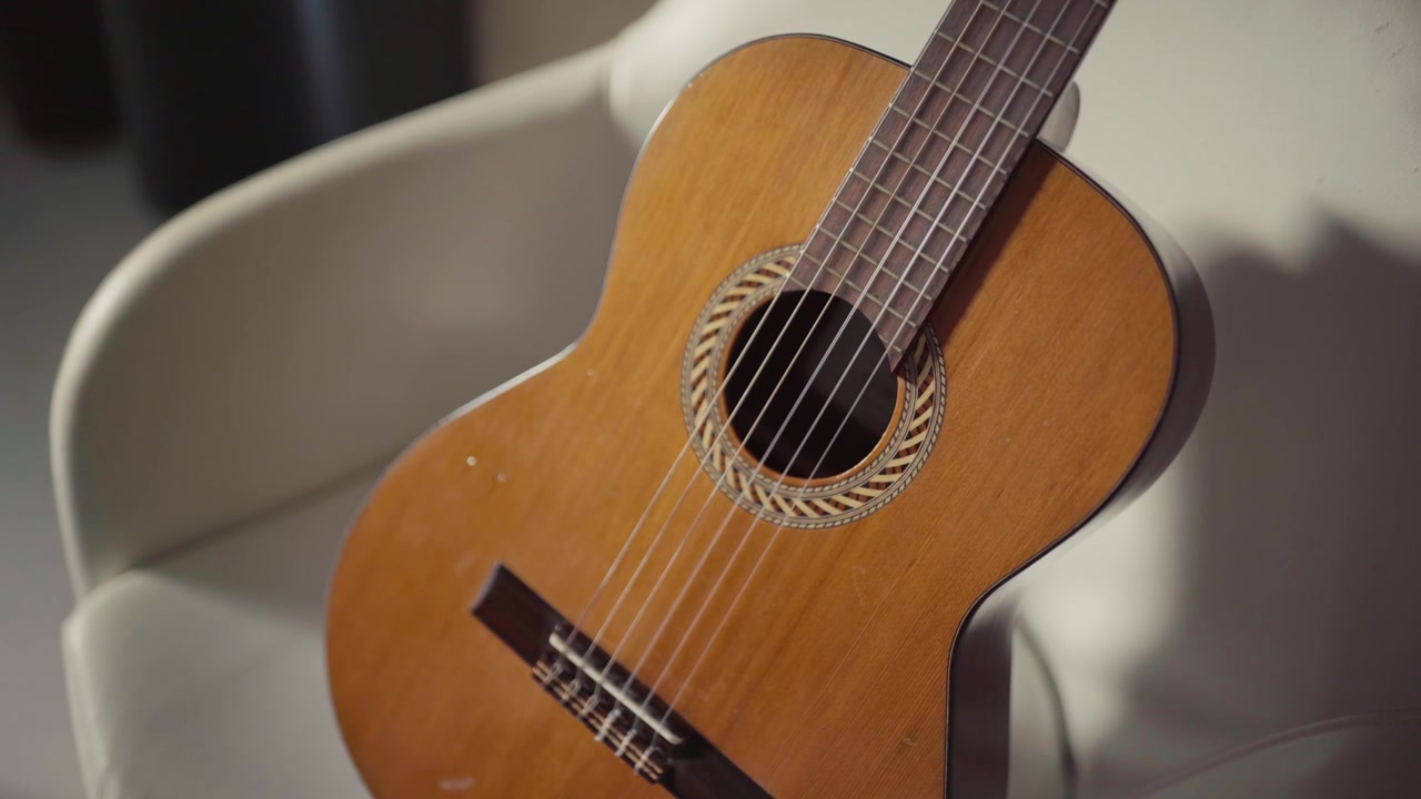 A wooden acoustic guitar rests on a white chair in soft lighting creating a warm and inviting feel