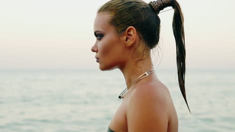 close up view of sexy woman with professional golden makeup and wet ponytail walking by the water on the beach then turning and