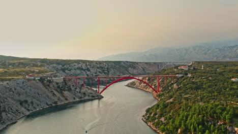 wide aerial shot of a big red bridge on a beautiful mountain scenery on sunset, camera descending