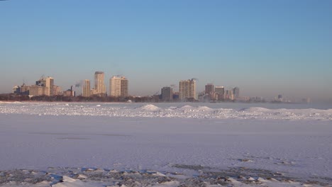 wind blowing snow across a frozen lake with a city skyline in background during winter chicago 4k