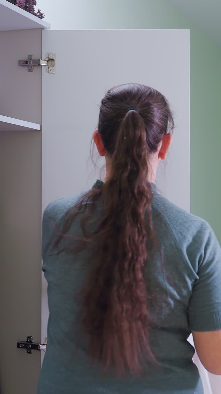 In well lighted clinical room woman therapist retrieves work attire from locker and walks toward x-ray machine adjusting uniform confidently surrounded by medical equipment desk and monitor